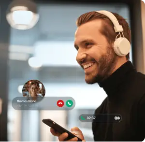 Un homme souriant portant des écouteurs blancs, tenant un smartphone en main avec un appel entrant de Thomas Blanc affiché sur l'écran.